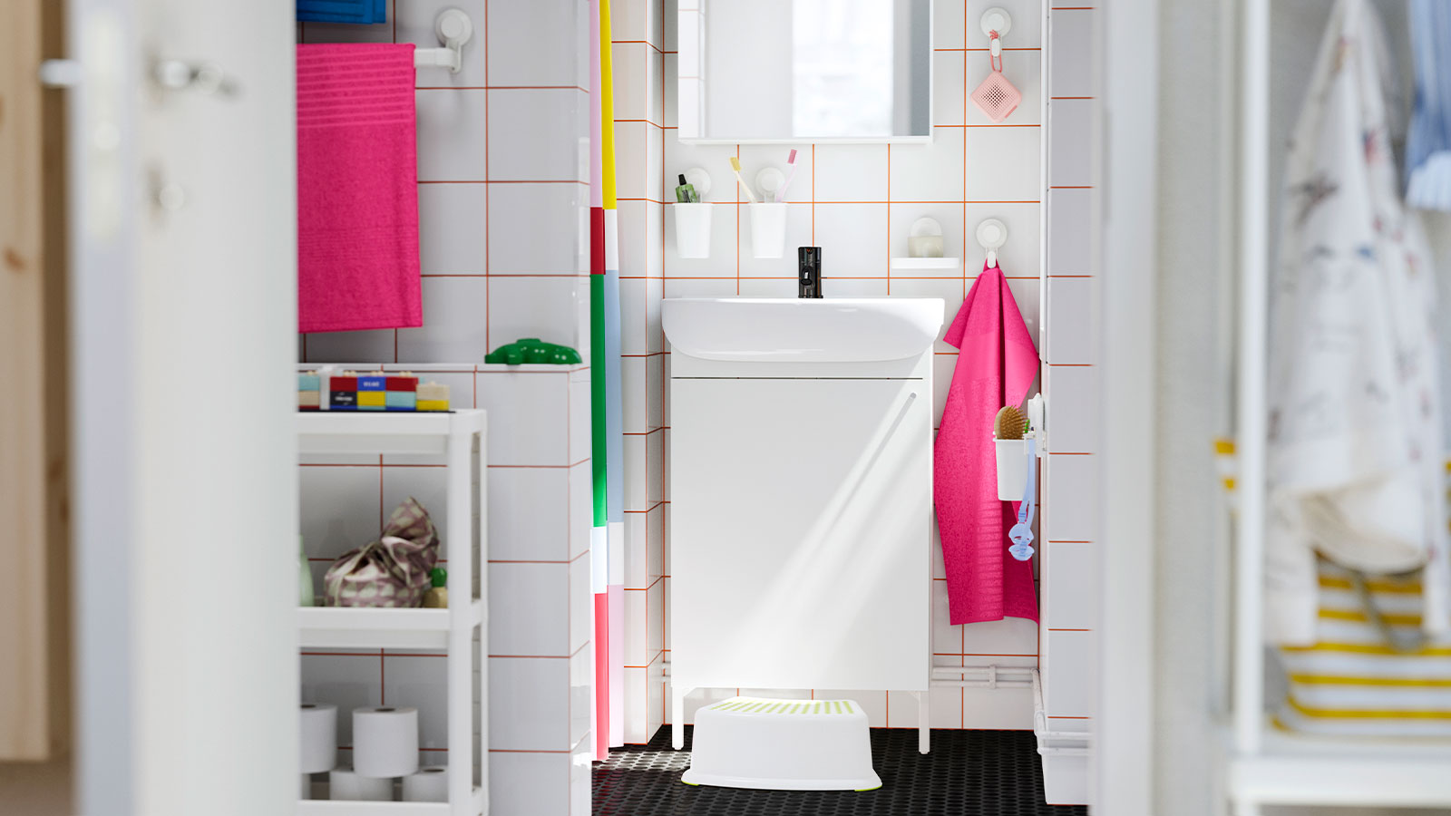  White bathroom with orange tiled grout. Pink towels, white step stool. Clean and functional atmosphere.