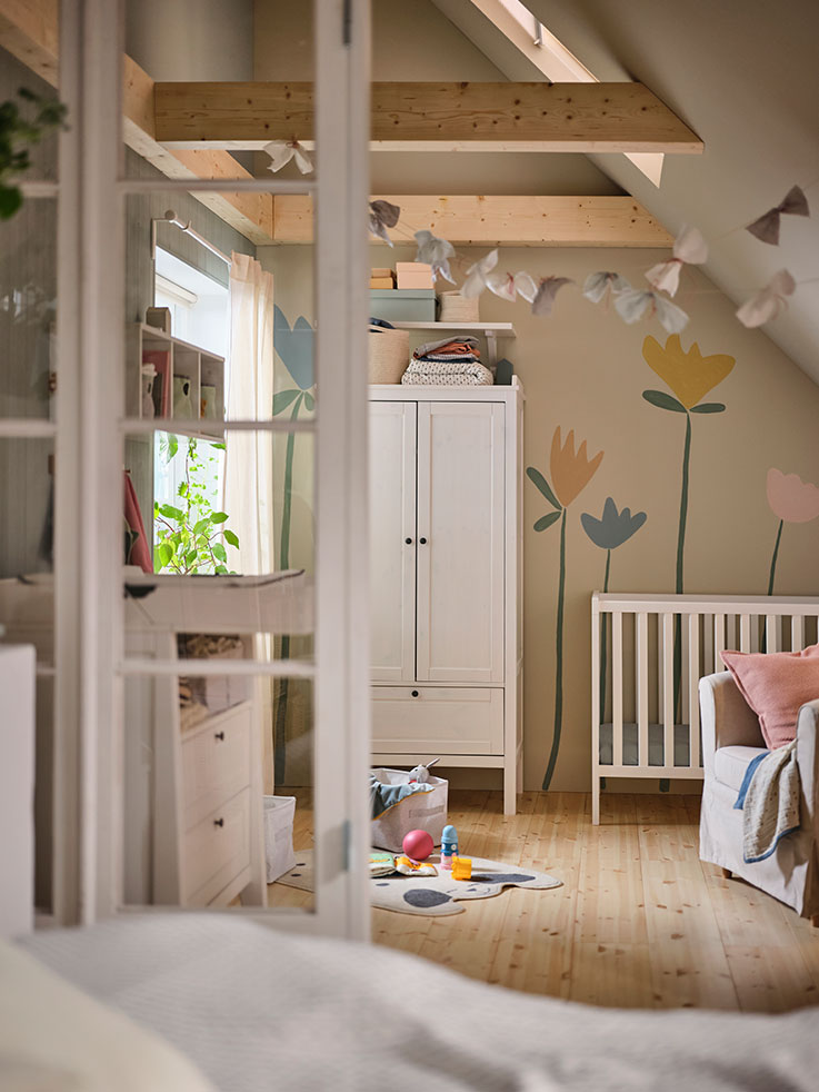 Una habitación de bebé, un cambiador frente a una ventana, una estantería modular, un armario junto a una cuna y juguetes en el suelo junto a una cortina.
