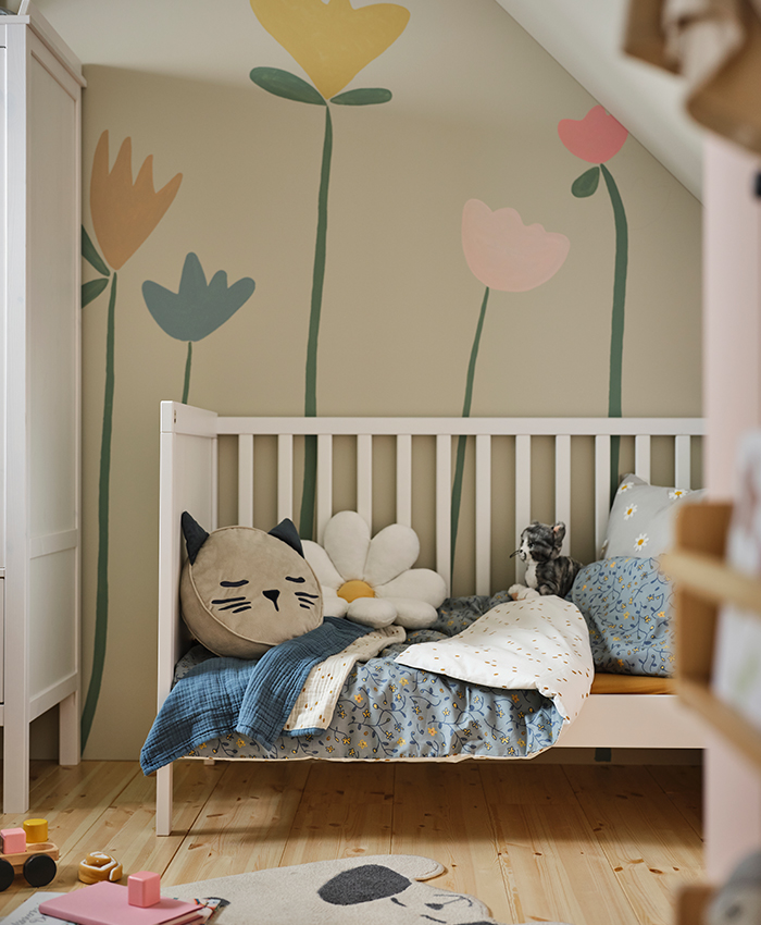Un cuarto de bebé con una cuna SUNDVIK, una colcha GULDVÄVARE encima y un BARN...