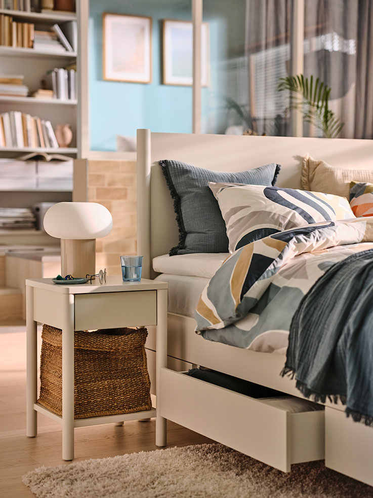 A TONSTAD nightstand with a DEJSA lamp on top, next to a TONSTAD bed in a bedroom.