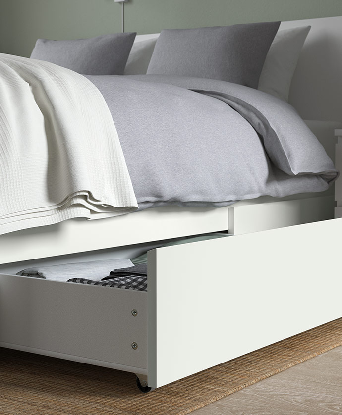 White bed with built-in storage and open lower drawer showing neatly folded bedding.
