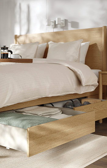 Wooden bed with open storage drawer, light-colored bedding, and a coffee tray on top.