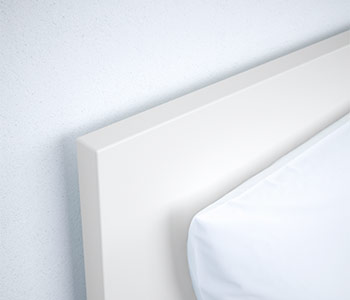 White headboard with clean lines next to a mattress with a white fitted sheet.