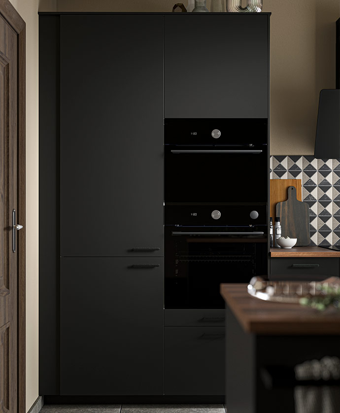 Modern kitchen with tall black cabinets and built-in ovens, wooden countertop, and a wall decorated with geometric tiles in white, grey, and black.