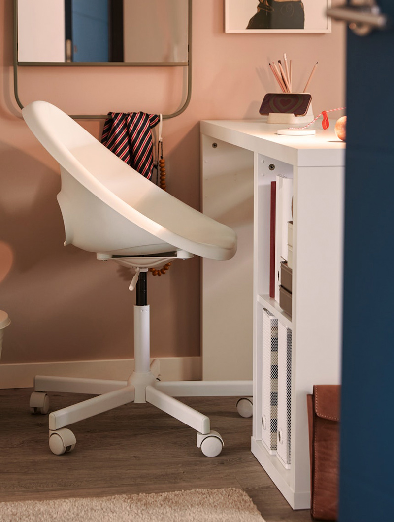 Silla de escritorio blanca con ruedas, en cuarto rosa. Escritorio blanco con objetos. Ambiente de estudio.