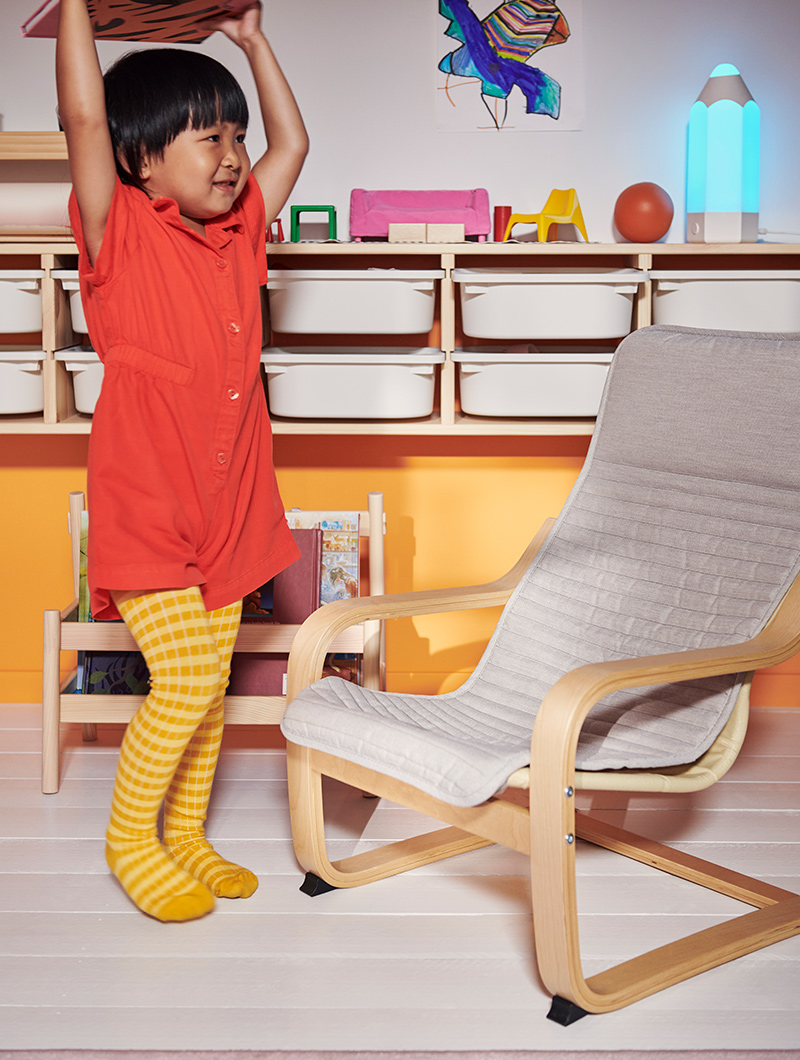  A child standing next to a POÄNG kid's armchair.