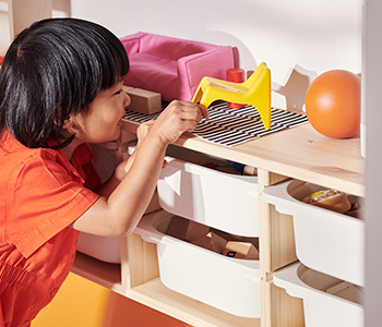  A girl placing a toy on a TROFAST wall storage