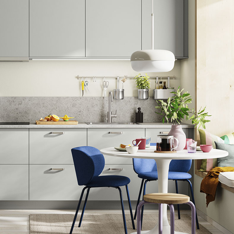 Cocina moderna gris y blanca, mesa redonda con sillas azules. Ambiente luminoso y contemporáneo.