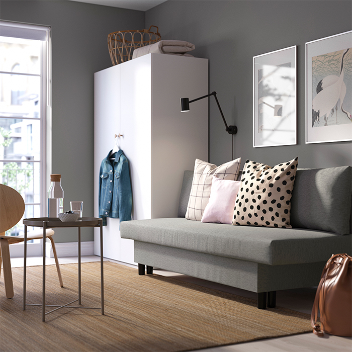 Una sala moderna y acogedora con un sofá gris, cojines estampados y luz natural entrando por la ventana.