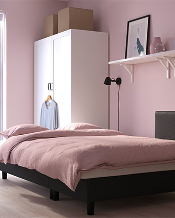 Un dormitorio acogedor con paredes rosas, una cama bien hecha, un armario blanco y objetos decorativos en una repisa.