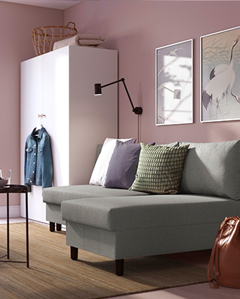 Una esquina acogedora de sala con un sofá gris, cojines decorativos, cuadros en la pared y un armario blanco contra una pared rosa.