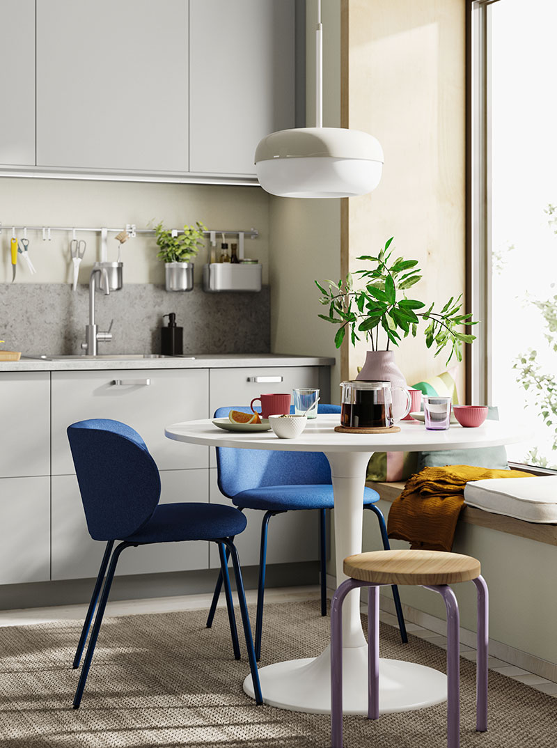 Cocina moderna gris y blanca, mesa redonda con sillas azules y taburete lila. Ambiente luminoso.