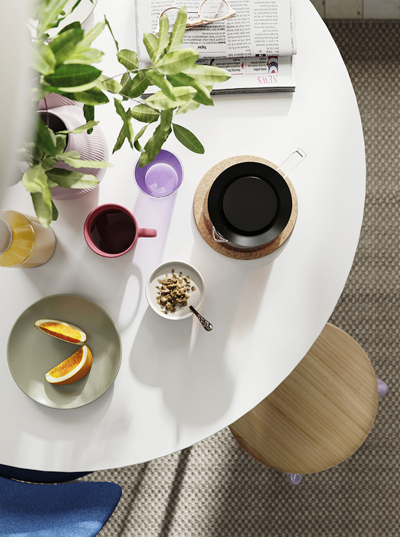 Mesa redonda blanca con desayuno, jugo, café y plato de frutas. Ambiente matutino y fresco.