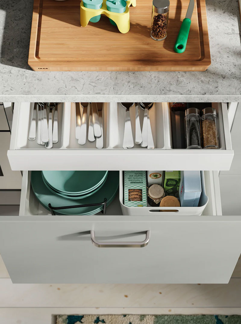 Cajones de cocina abiertos con cubiertos, platos y especias organizados. Ambiente de cocina funcional.