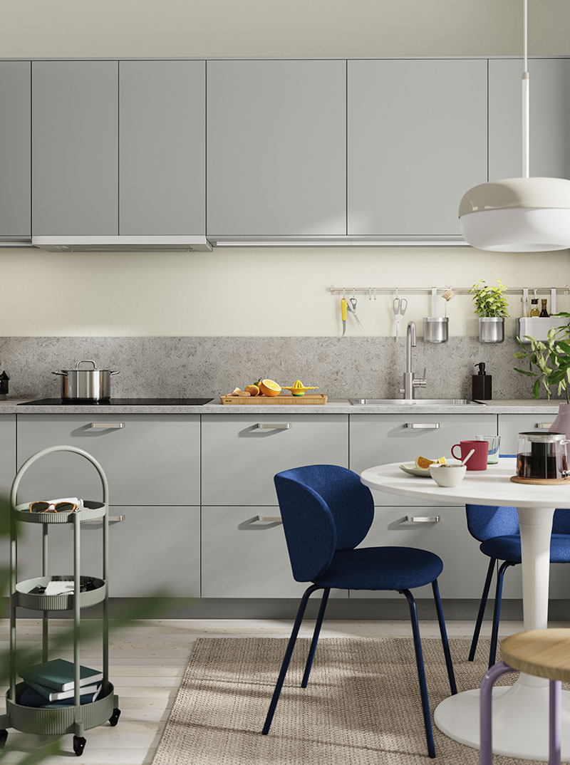 Cocina moderna con gabinetes grises, mesa redonda blanca y sillas de terciopelo azul. Luminosa.