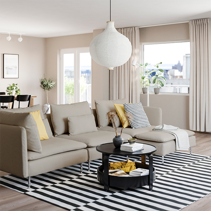 Sofá gris de estilo moderno en sala iluminada, con decoración en tonos beige, mesa de centro redonda negra y alfombra de rayas blancas y negras.