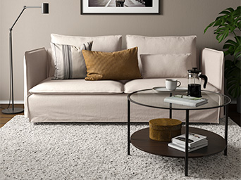 Sofá gris de estilo moderno en sala iluminada, con decoración en tonos beige, mesa de centro redonda negra.