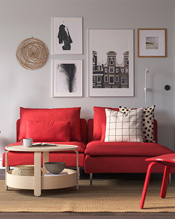 Sofá moderno rojo con cojines rayados y con puntos, mesa de centro redonda de madera estilo moderno y cuatro cuadros con fotos en la pared.