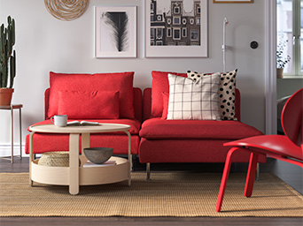 Sofá moderno rojo con cojines rayados y con puntos, mesa de centro redonda de madera estilo moderno y cuatro cuadros con fotos en la pared.