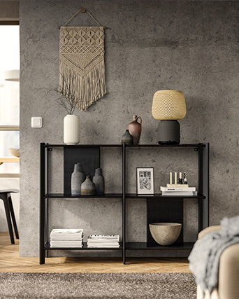 Low black sideboard with decorative items against an industrial-style grey wall.