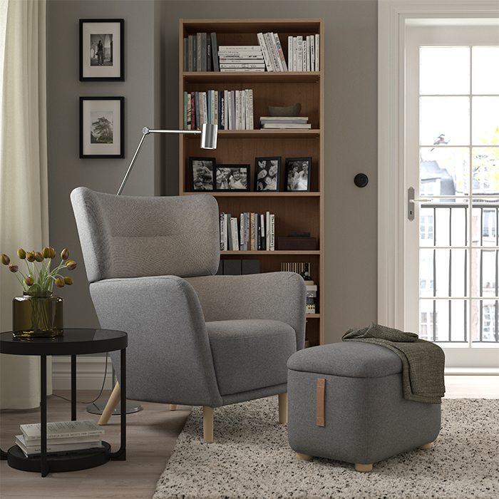 Grey upholstered armchair with headrest in a modern setting, with a upholstered stool.