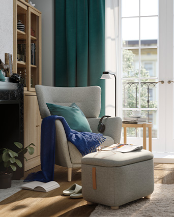 Grey upholstered armchair with headrest in a modern setting, with a upholstered stool.