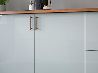 Close-up of glossy white lower kitchen cabinets with metal handles and wooden countertop.