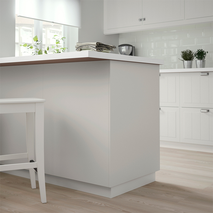 Bright white kitchen with central island, stool, smooth countertop, and decorative plants on light wood flooring.