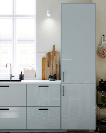 Kitchen with glossy white cabinets, sink by the window, and wooden cutting boards resting on the countertop.