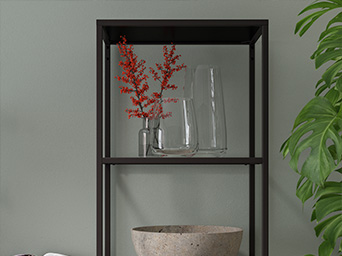 A dark metal shelf displays clear glass vases, one with vibrant red flowers, and a textured beige bowl, beside a green plant.