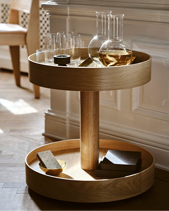 A stylish wooden bar cart holds glassware, decanters, and books in a sunlit room.