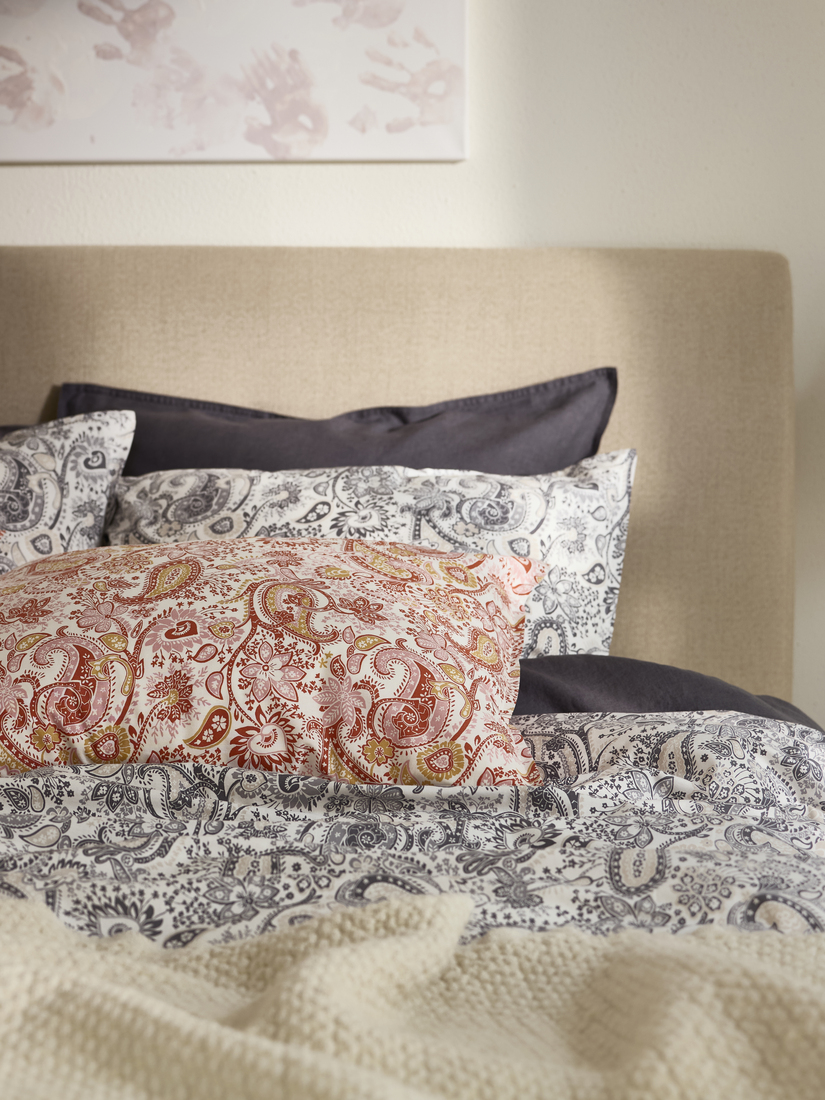 Bed with a white comfort and a Paisley pattern in pink and orange.