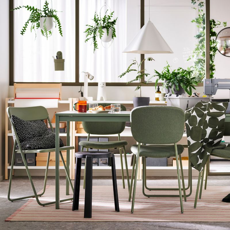 A bright, natural dining/workspace with green chairs, matching table, and plants.