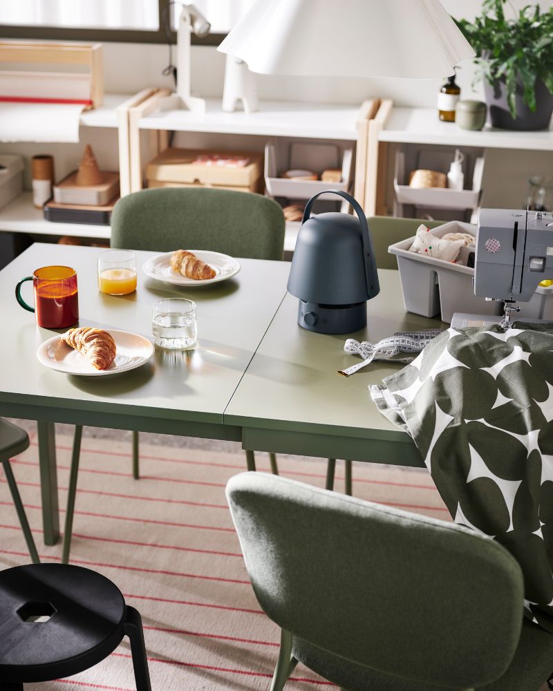 A serene dining/work area with green table and chairs, natural accents, and patterned textiles.