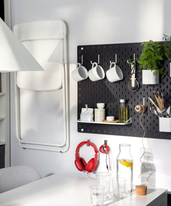 Black pegboard wall organizer with mugs, plants, and red headphones. Functional and modern.