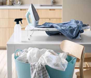 Laundry setting with iron, denim clothes, spray bottle, and light blue basket with white laundry.