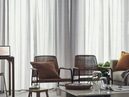Modern living room with rattan armchairs, sheer curtains, and a decorated coffee table.