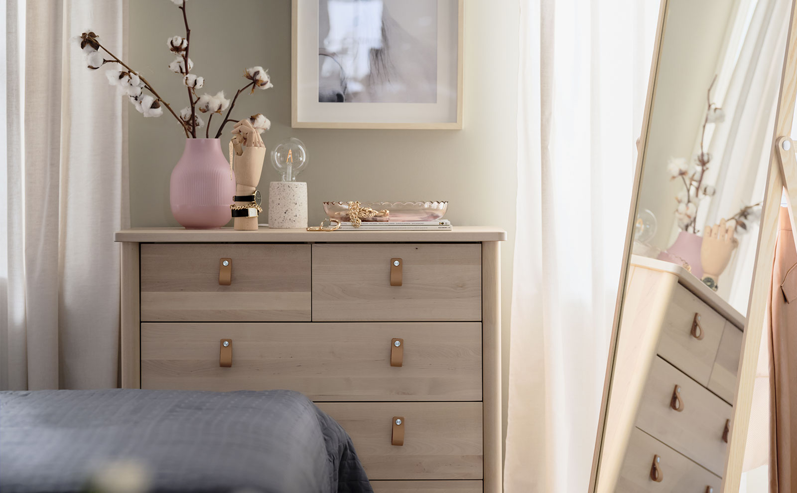 Five-drawer vertical chest of drawers in pine,  has a vase with flowers, and blurred floor mirror in the foreground