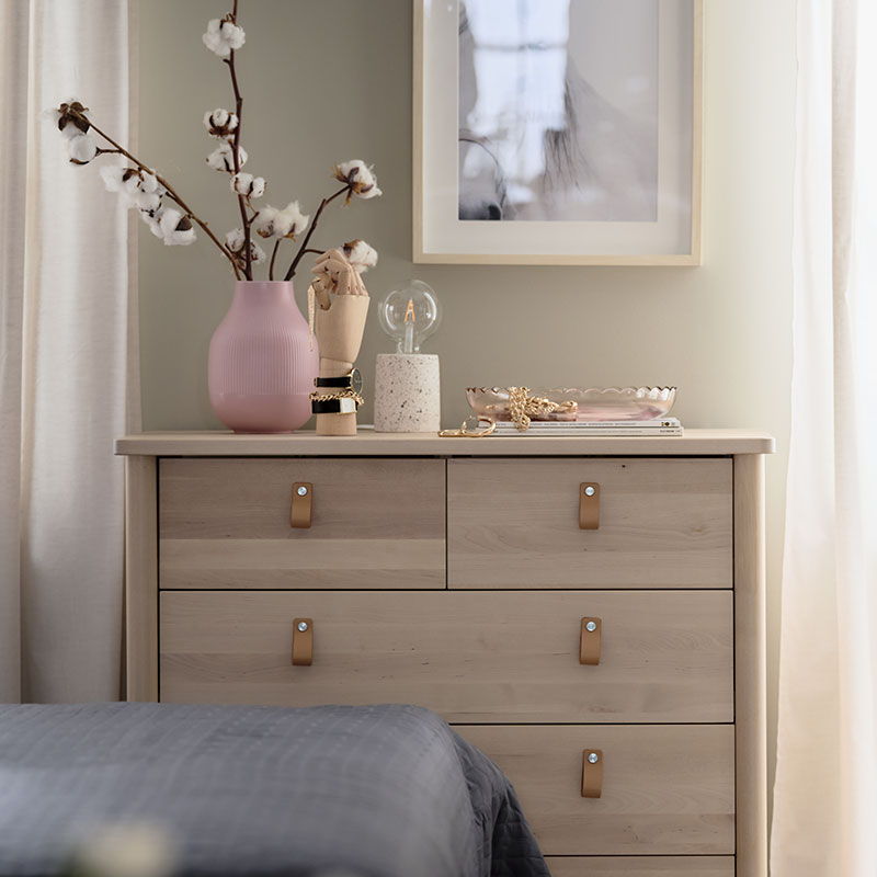 Five-drawer vertical chest of drawers in pine,  has a vase with flowers, and blurred floor mirror in the foreground