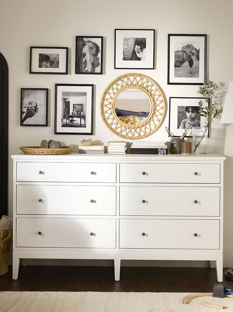 Two-drawer chest with small round rattan mirror, black-framed wall art.
