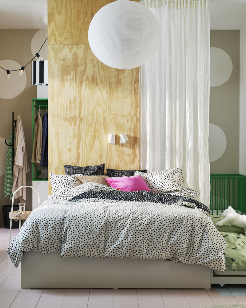 A VIHALS double bed with 4 storage drawers in a bright bedroom with a DYTÅG curtain divider and a green cot behind it.