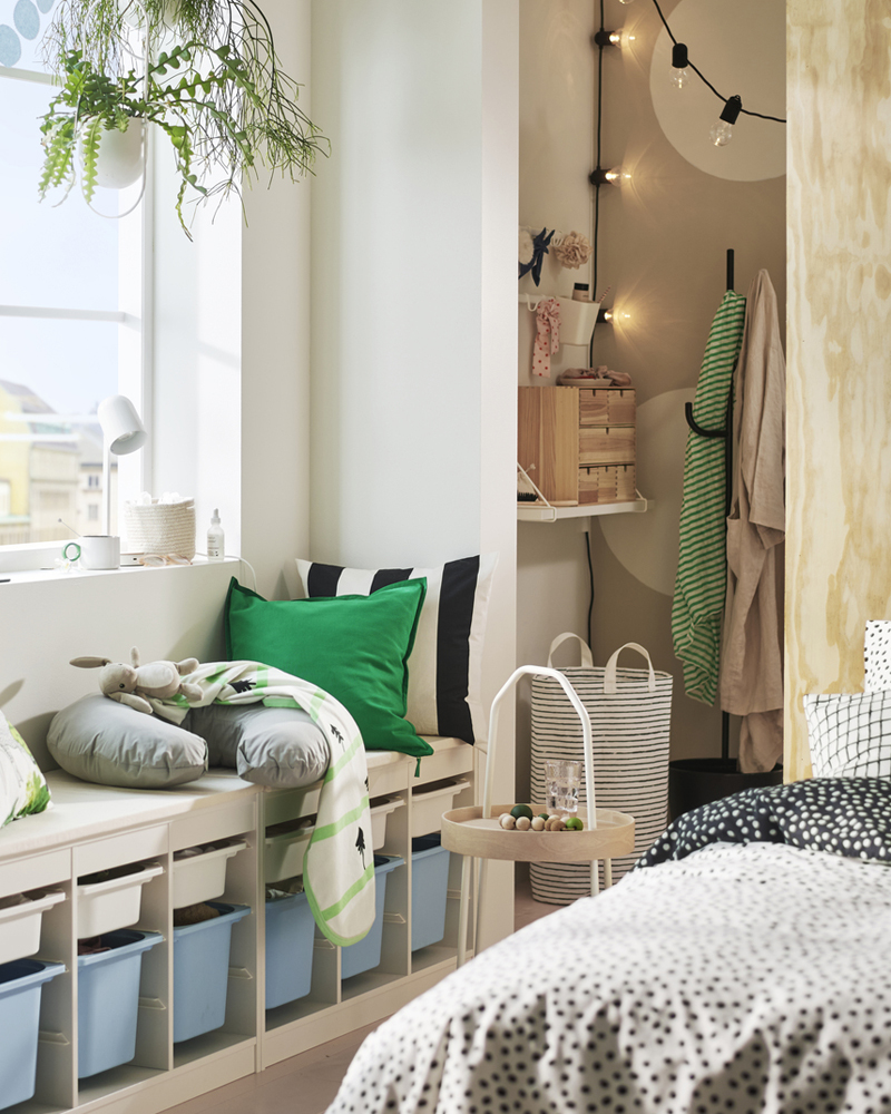 A cosy room featuring a TROFAST frame in white holding colourful storage boxes and with cushions on top under a sunny window.