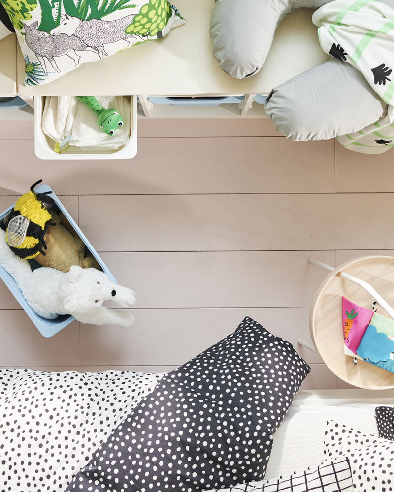 A light blue TROFAST storage box on the floor is filled with plush toys, beside a white TROFAST frame with cushions on top.