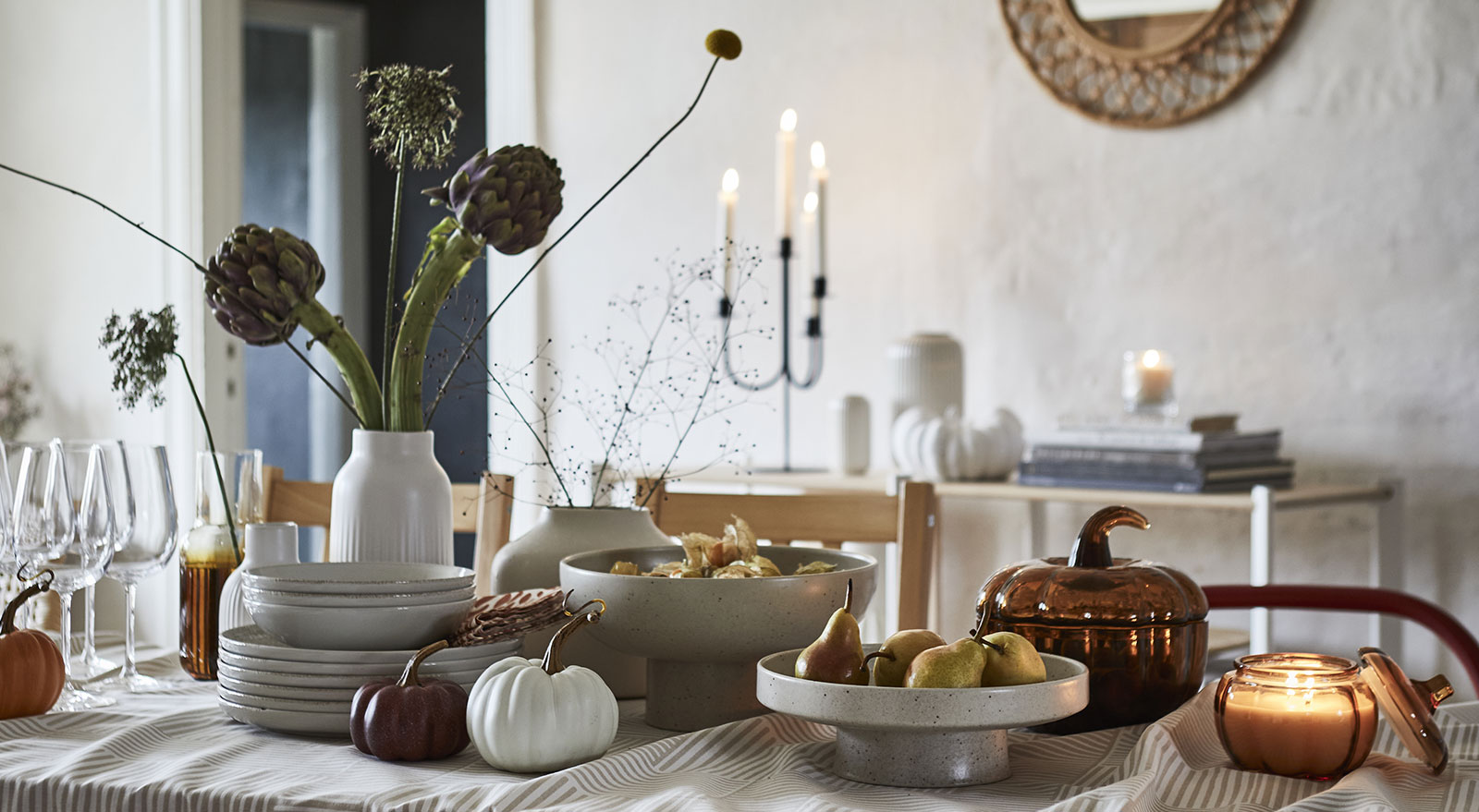 Un soporte y un cuenco de color beige claro de HÖSTAGILLE sirven para servir fruta en una mesa de comedor bien puesta.