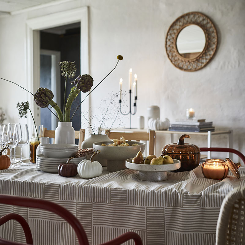 Un soporte y un cuenco de color beige claro de HÖSTAGILLE sirven para servir fruta en una mesa de comedor bien puesta.