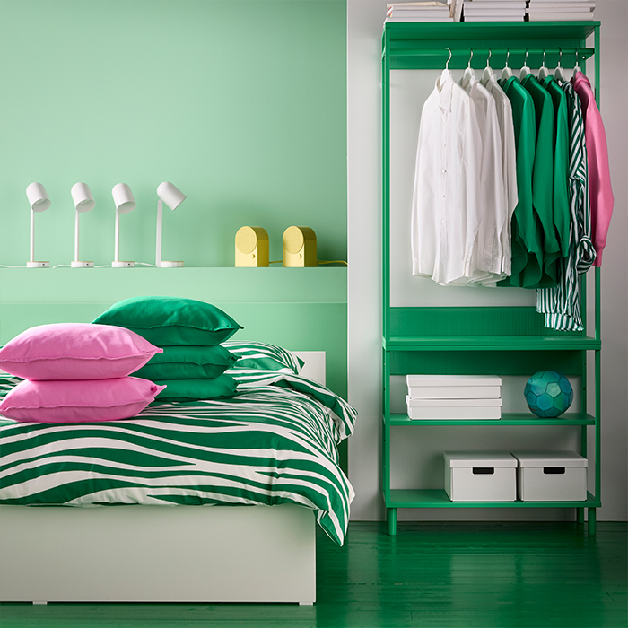 Dormitorio moderno IKEA con cama verde a rayas, almohadas rosas y armario abierto verde. Soluciones de almacenaje para un espacio organizado y con estilo.