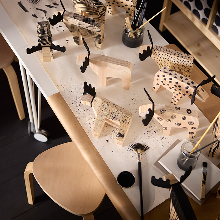 Mesa de manualidades IKEA con figuras de alces de madera y materiales de pintura. Ideas para proyectos creativos en casa.