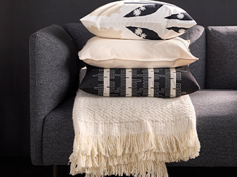 Cojines y manta IKEA apilados en sofá gris. Textiles suaves y con patrones para añadir confort y estilo a tu salón.