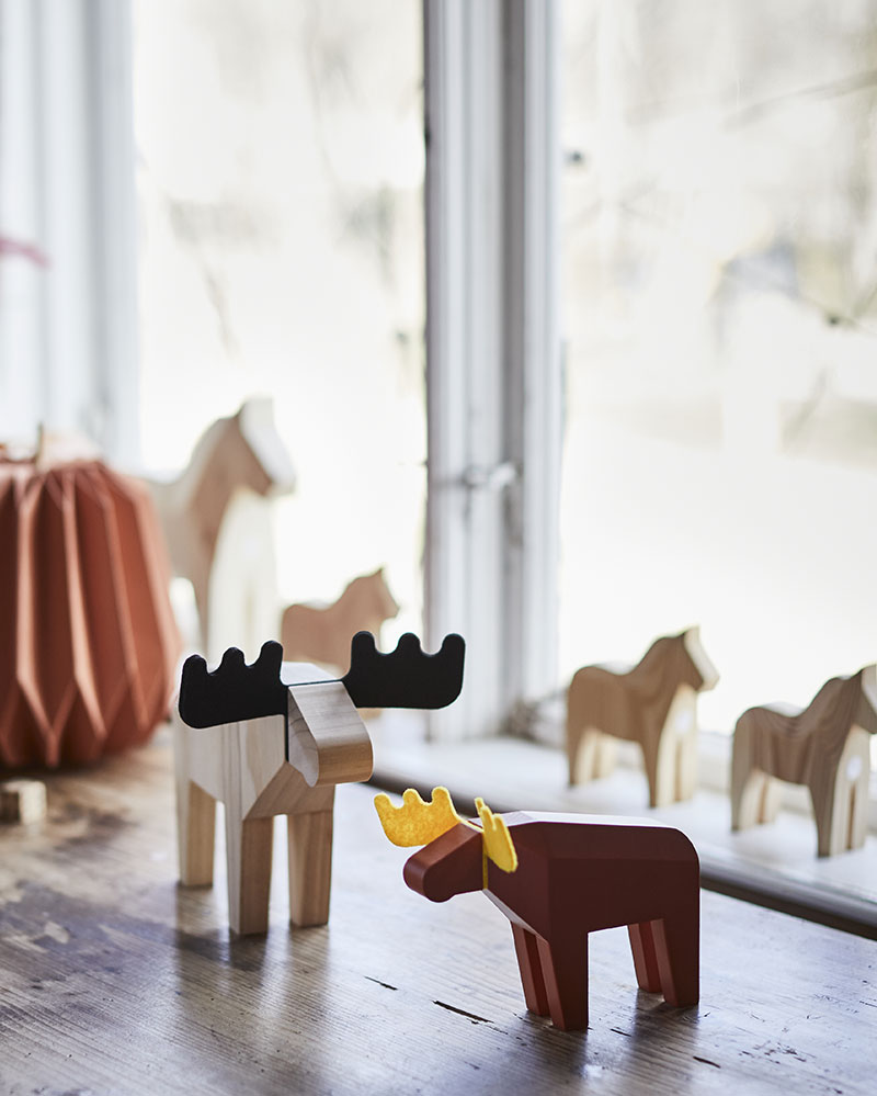 Dos figuras decorativas de alces de HÖSTAGILLE se colocan sobre una mesa de madera, rodeadas de adornos otoñales y luz natural.