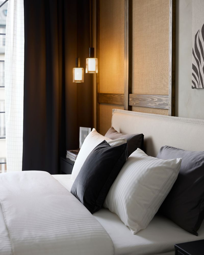 A hotel bed has rows of pillows and white, sateen-woven NATTJASMIN duvet cover and pillowcases that are discreetly striped.
